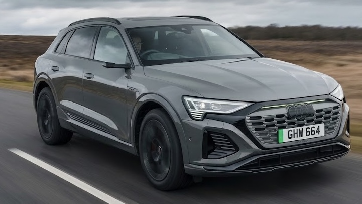 Electric grey Audi Q8 e-Tron SUV with a UK number plate driving along paved road through grassy landscape