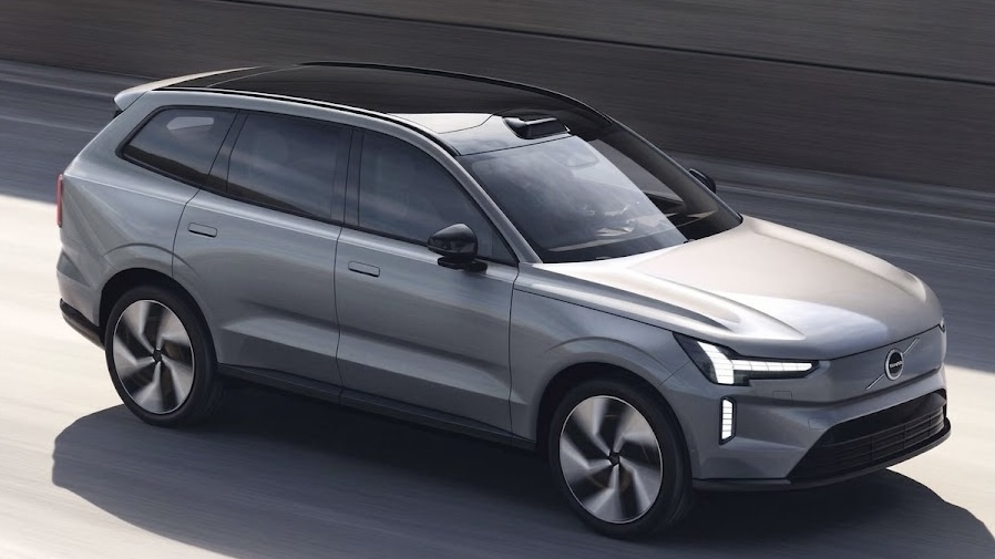 Electric grey Volvo EX90 SUV with black roof captured in motion as it drives on asphalt road